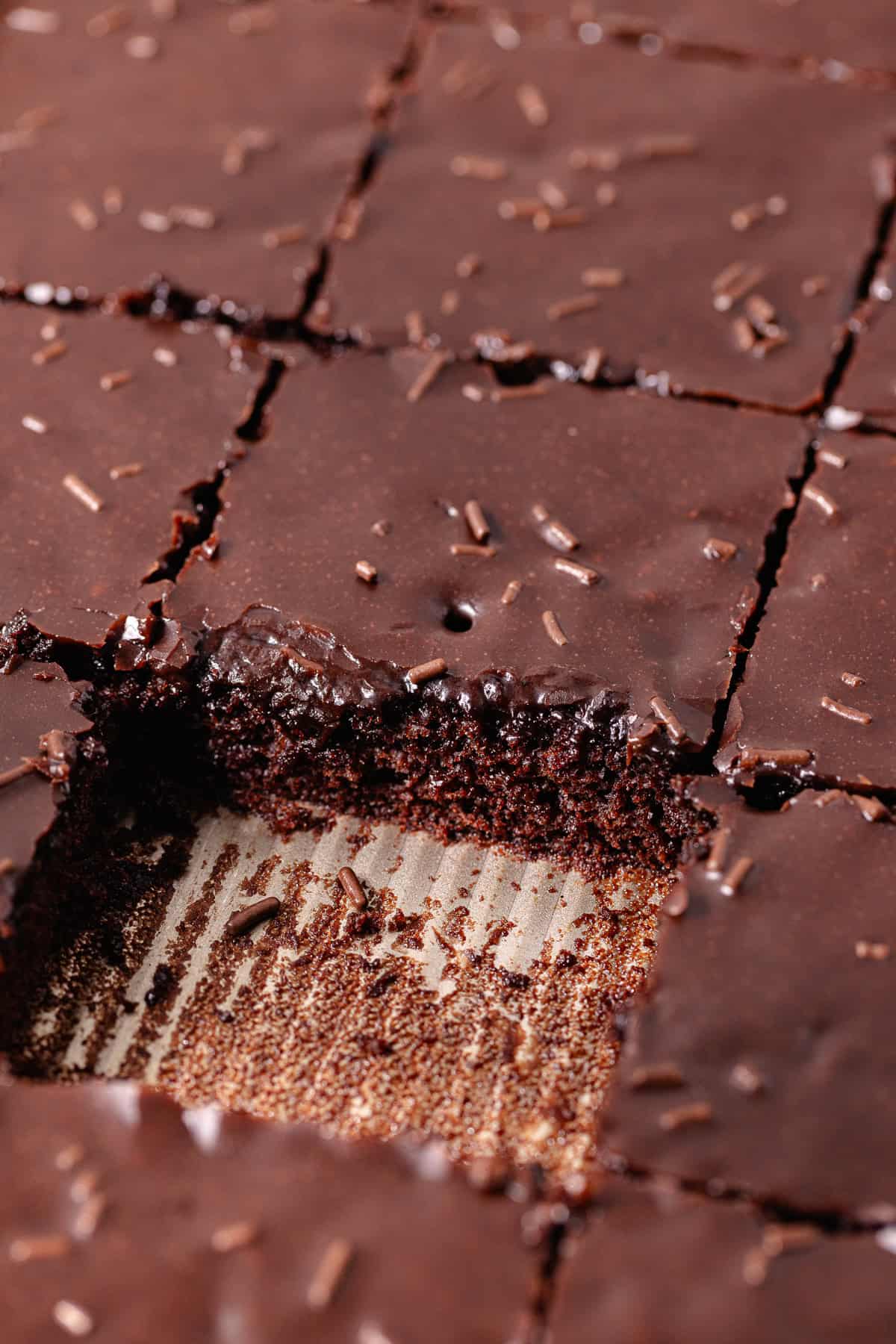 Dark chocolate sheet cake, also known as Texas sheet cake, is topped with a dark chocolate icing and chocolate sprinkles, and cut into squares.