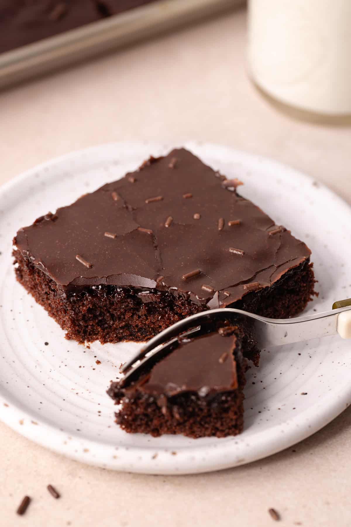 Dark chocolate sheet cake, also known as Texas sheet cake, is topped with a dark chocolate icing and chocolate sprinkles, is on a small dessert plate.