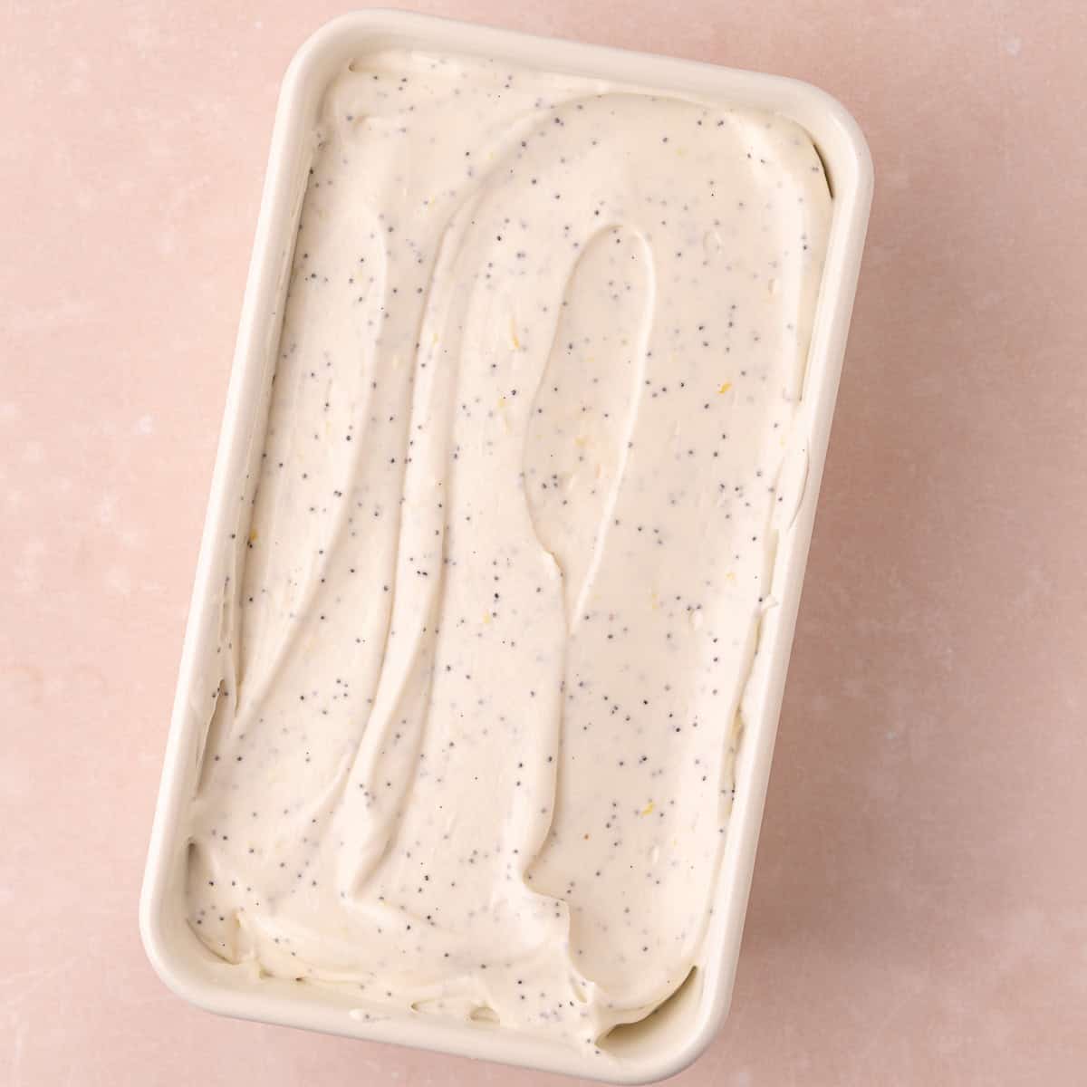 No-churn Lemon poppy seed ice cream is in a white loaf pan and ready to be frozen overnight.