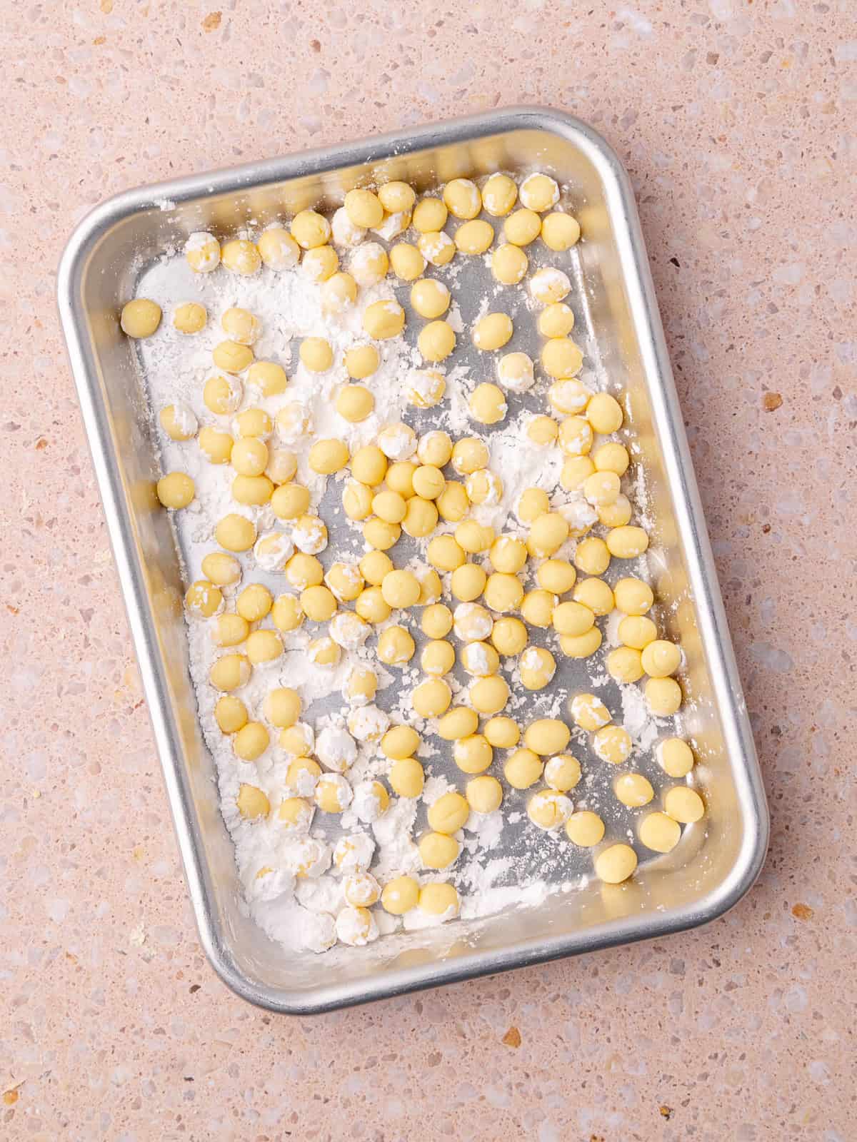 Homemade peach boba pearls are rolled into small balls are are added to a small baking tray with tapioca flour.