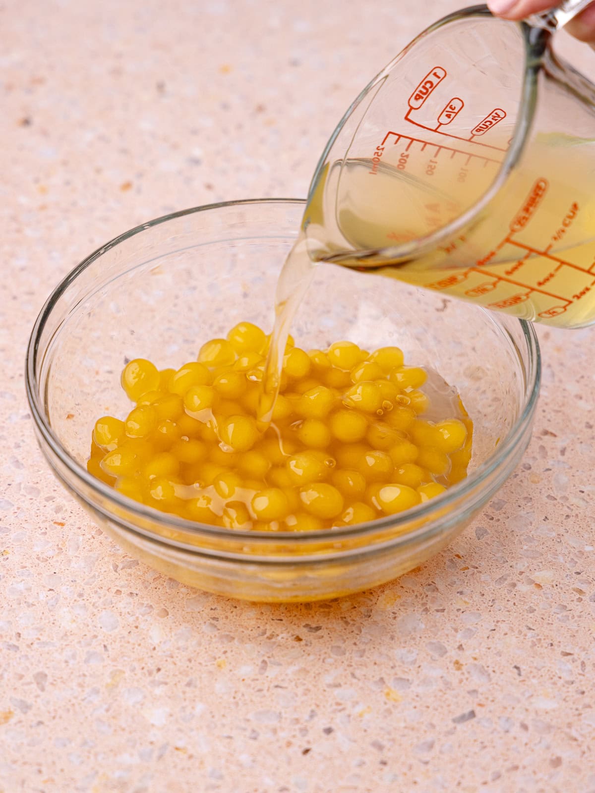 Peach syrup is mixed together in a small glass bowl with the cooked peach boba pearls.
