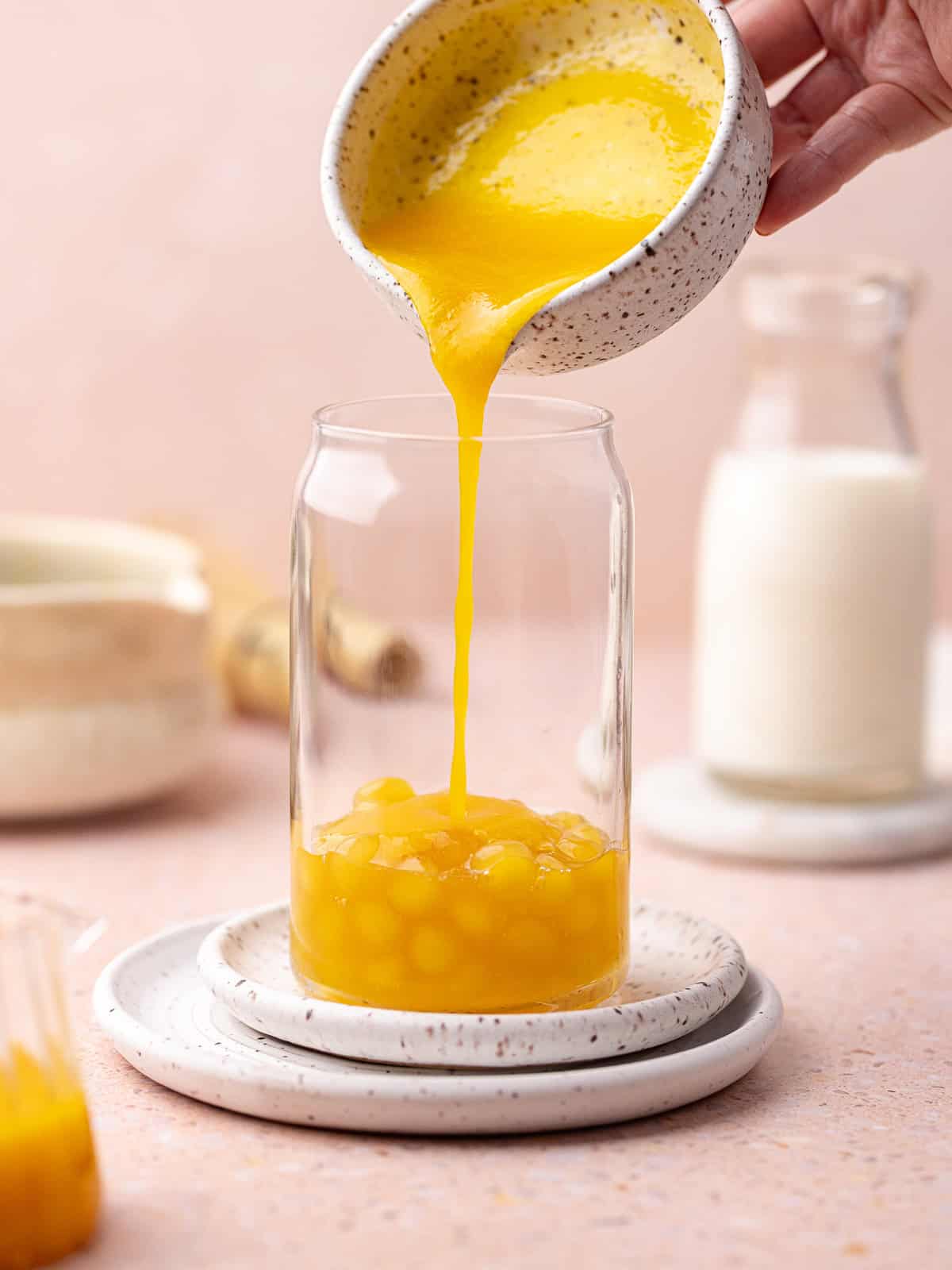 Peach puree is added over the homemade peach boba pearls sitting in the tall glass.
