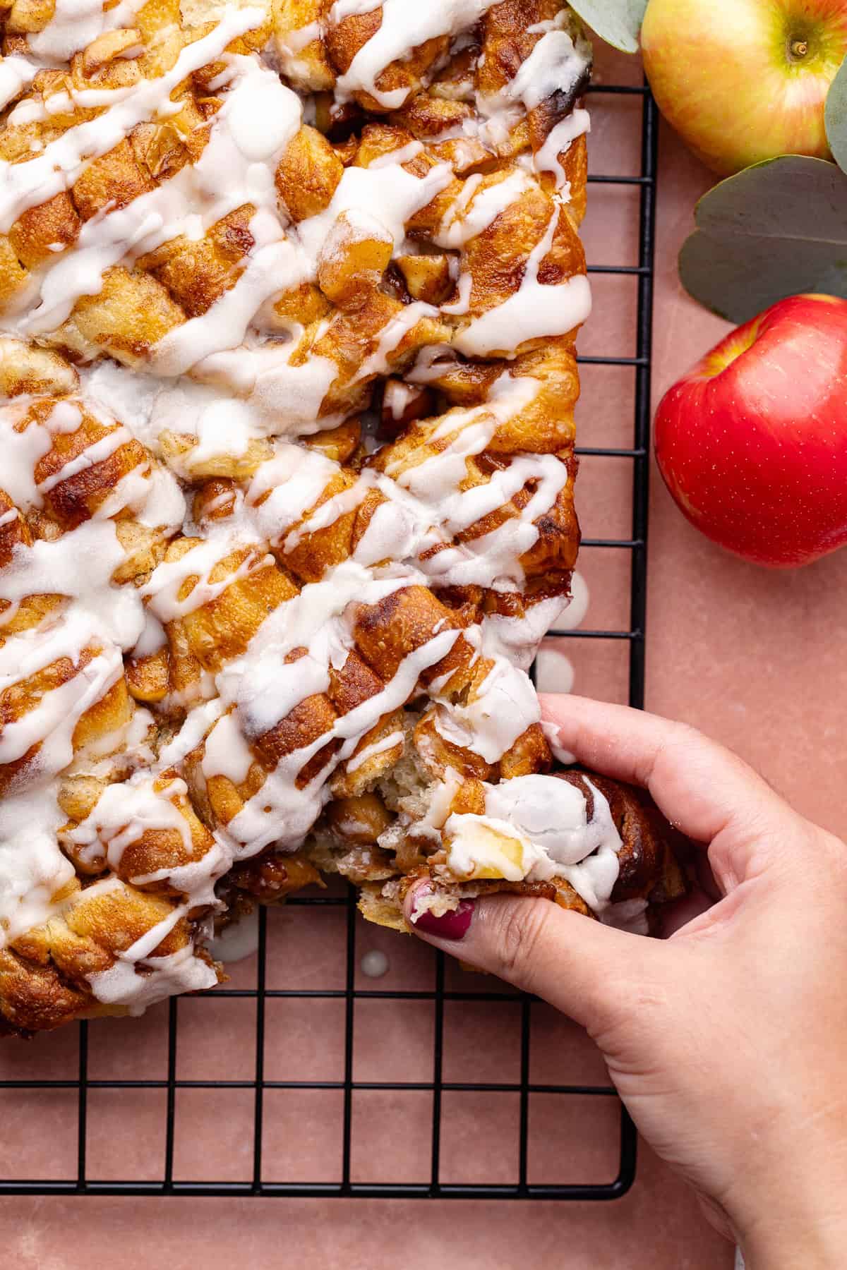 Soft and fluffy pull-apart apple fritter focaccia is topped with a delicious maple glaze and is sitting on a wire rack.