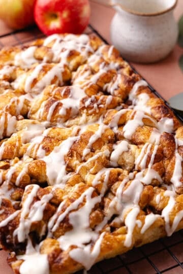 Soft and fluffy pull-apart apple fritter focaccia is topped with a delicious maple glaze and is sitting on a wire rack.