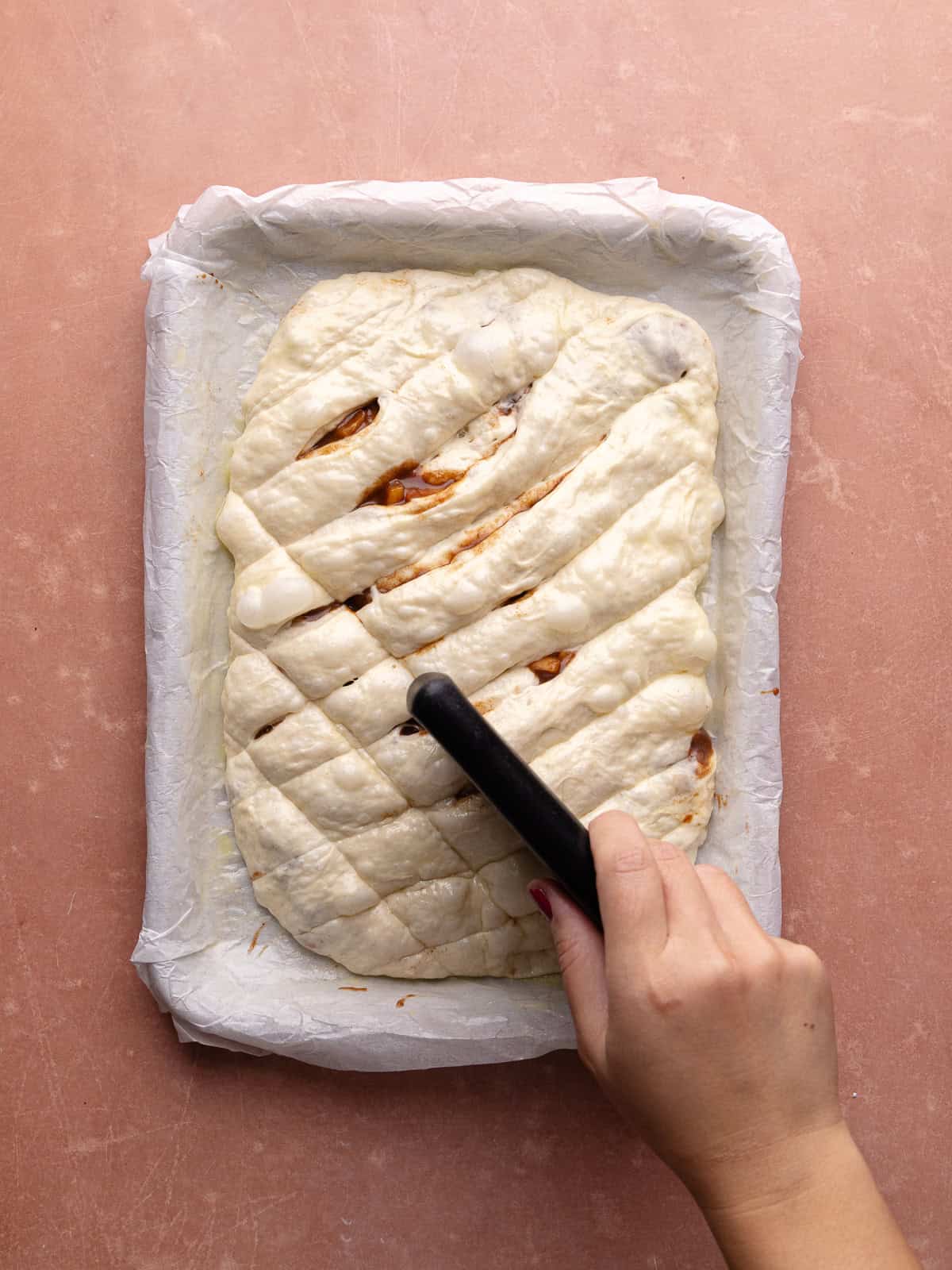 A metal bench scraper scores apple fritter focaccia loaf.