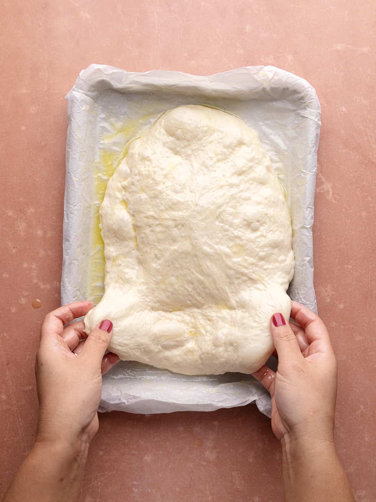 Focaccia dough is stretched to fill a lined quarter sheet pan.