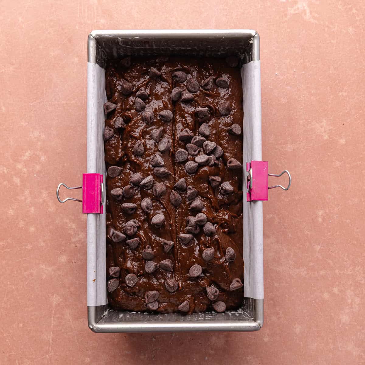 The chocolate pumpkin bread batter is transferred to a parchment paper lined metal 9x5 inch loaf pan. Chocolate chips are also added on top of the loaf before baking.