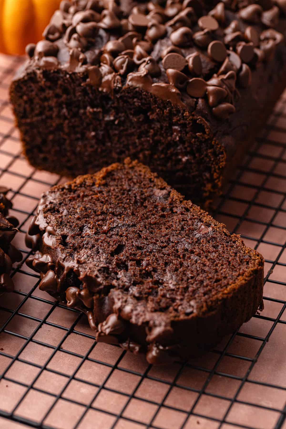 Super moist chocolate pumpkin bread studded with chocolate chips is sliced and sitting on a wire rack.