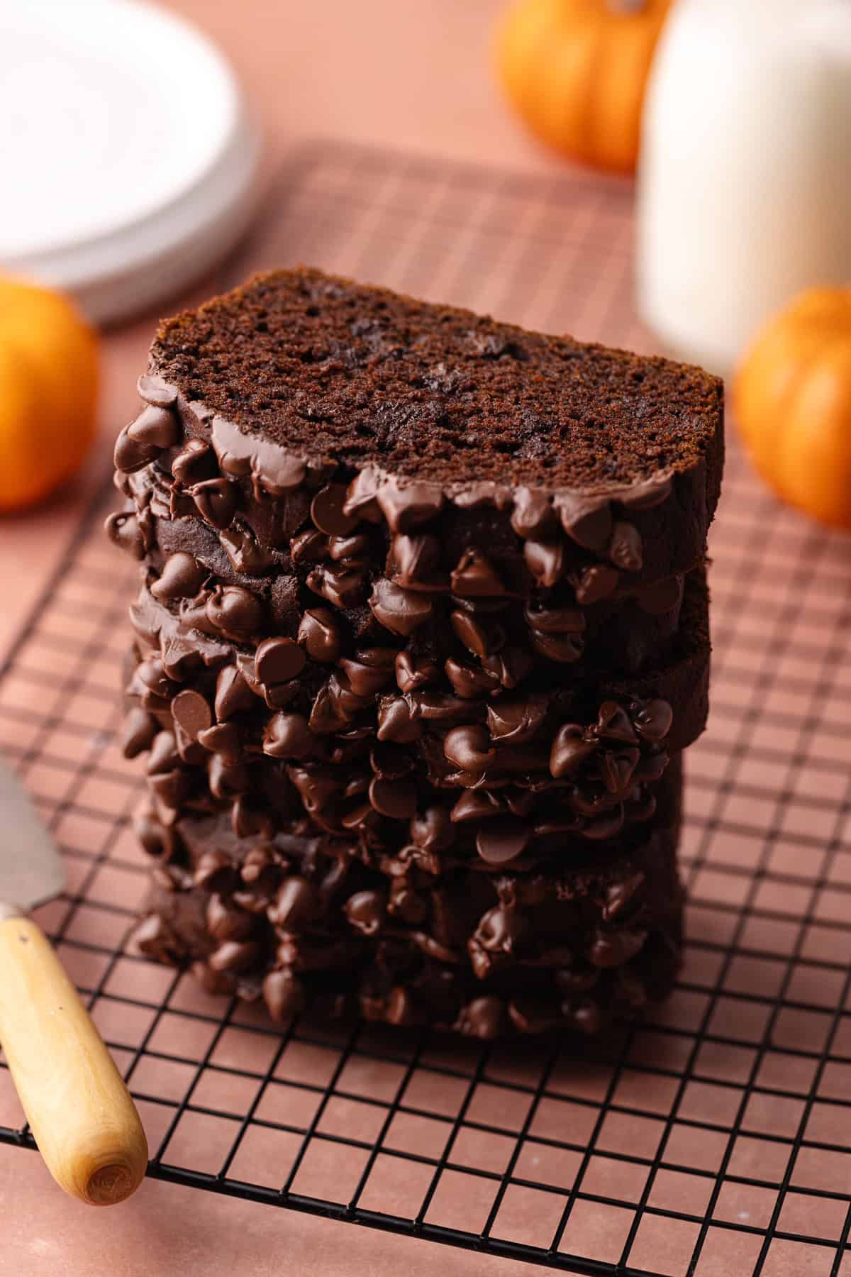 Slices of super moist chocolate pumpkin bread studded with chocolate chips are stacked on top of a wire rack.