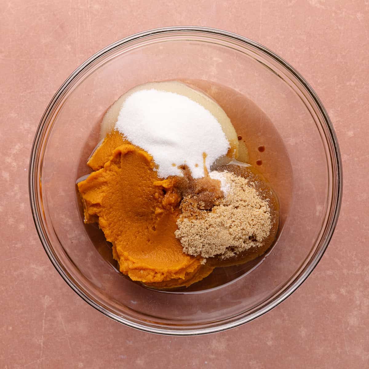 Oil, pumpkin puree, white sugar, brown sugar and vanilla are in a glass mixing bowl.