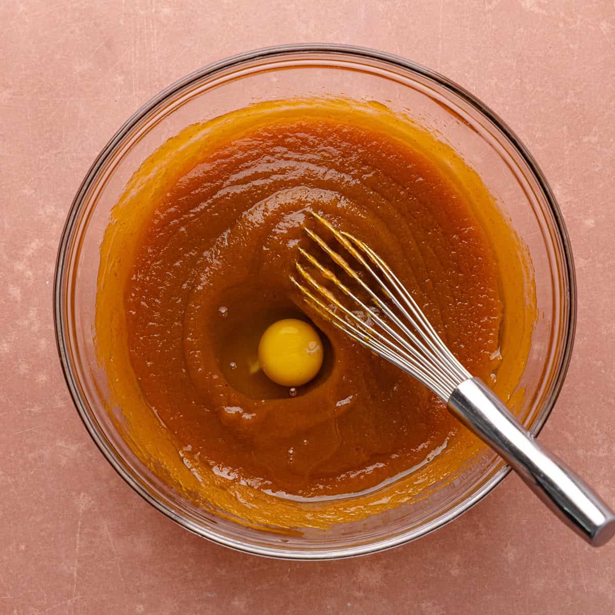 Oil, pumpkin puree, white sugar, brown sugar and vanilla are whisked together in a glass mixing bowl. An egg is added to the wet ingredients.