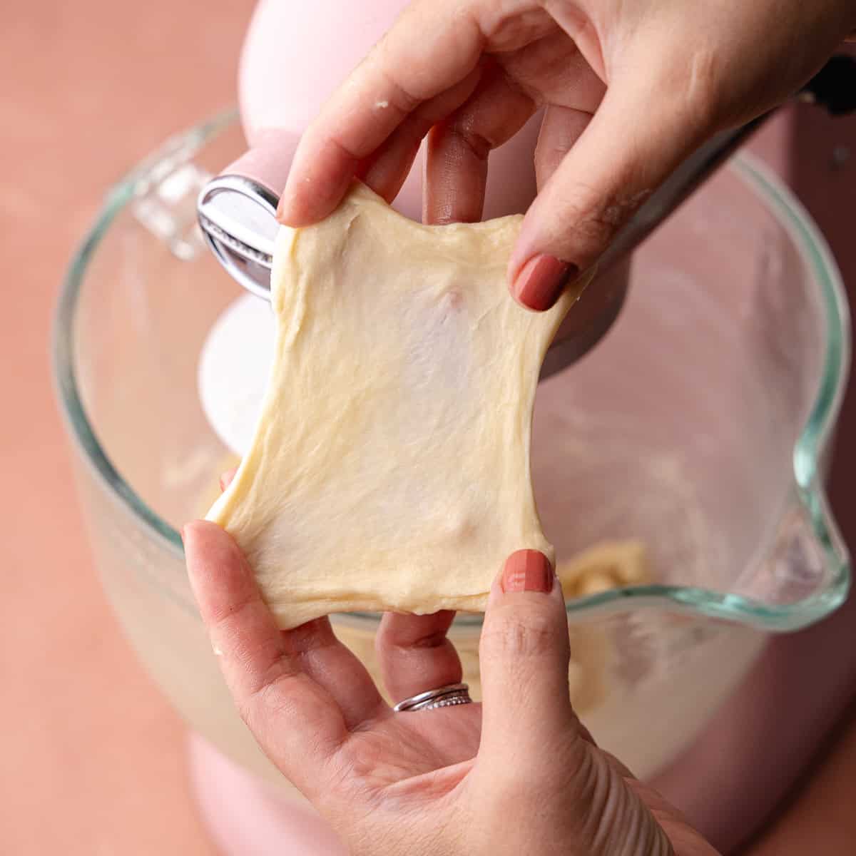 Milk bread donut dough is stretched into a window pane.