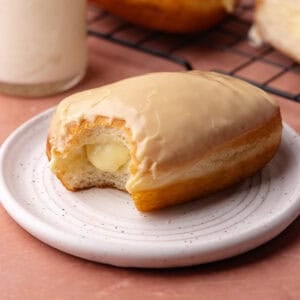 Maple bar donut filled with vanilla pastry cream and glazed in maple icing is sitting on a plate.