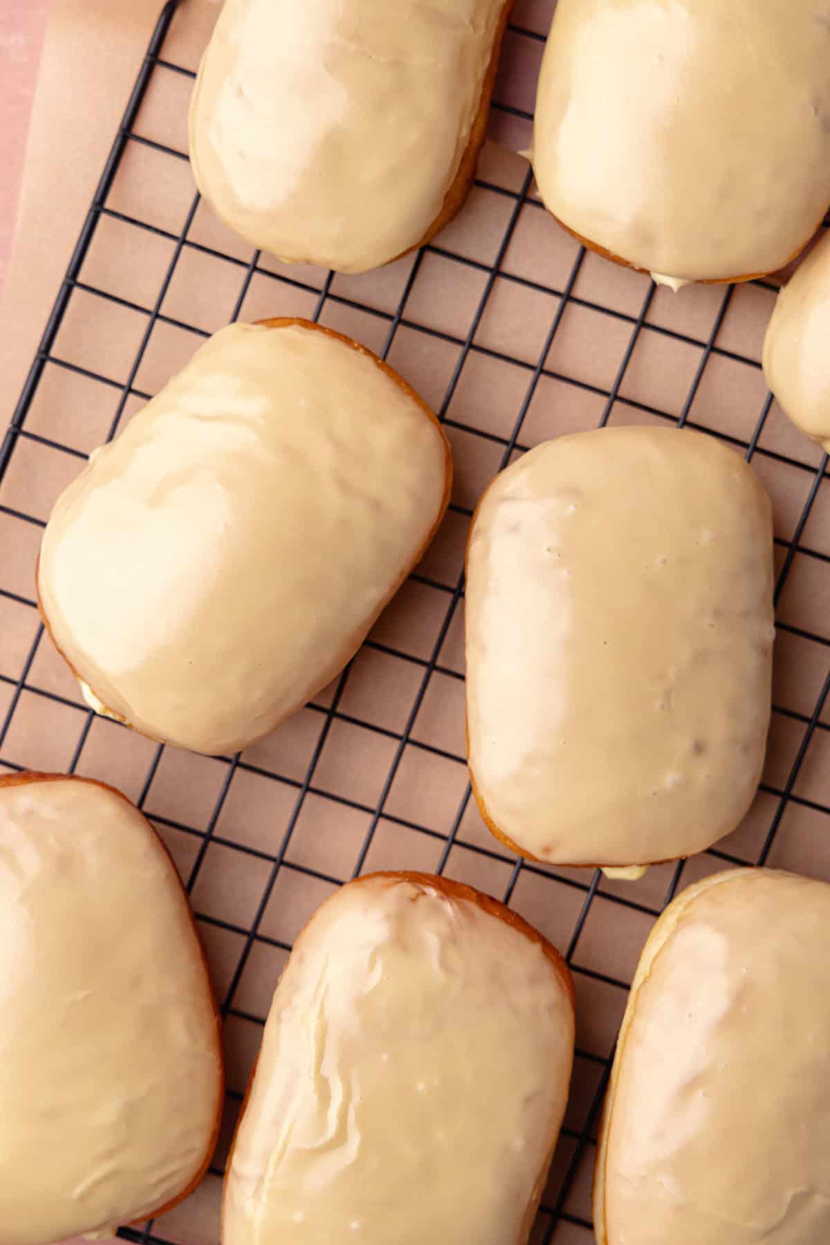 Maple bar donuts are filled with vanilla pastry cream and glazed in maple icing and sitting on a wire rack.