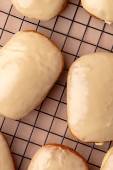 Maple bar donuts are filled with vanilla pastry cream and glazed in maple icing and sitting on a wire rack.