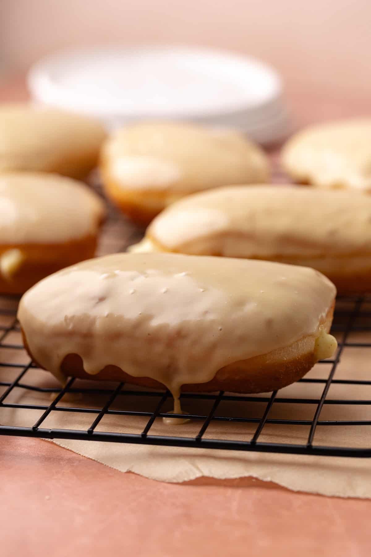 Maple bar donuts are filled with vanilla pastry cream and glazed in maple icing and sitting on a wire rack.