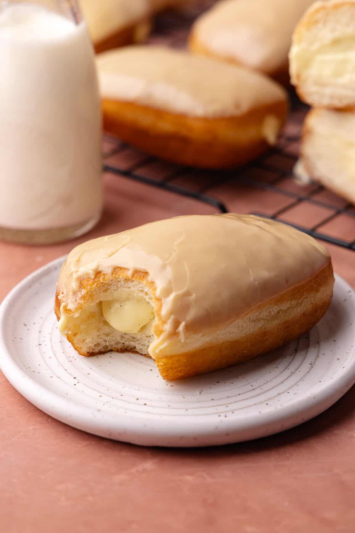 Maple bar donut filled with vanilla pastry cream and glazed in maple icing is sitting on a plate.