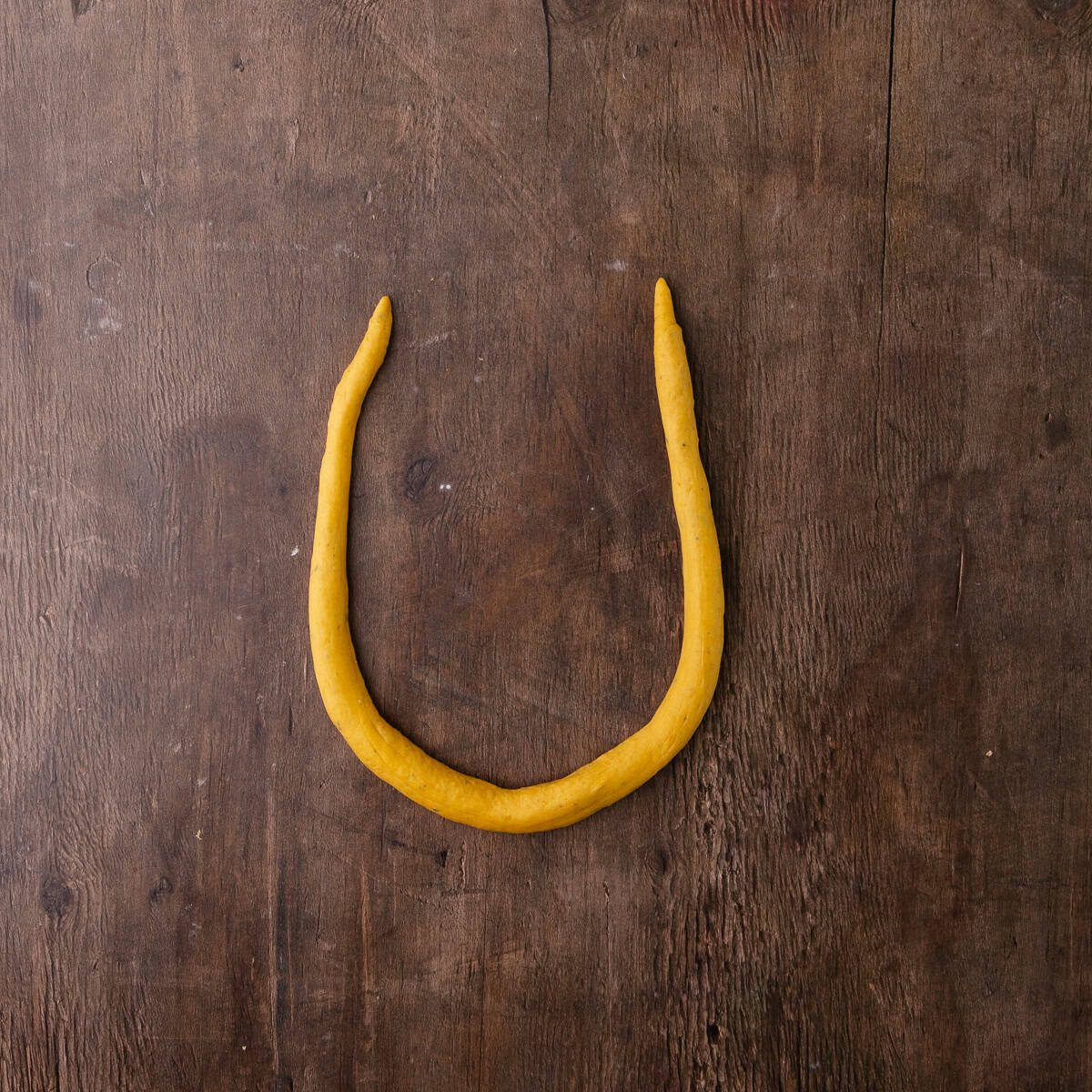 Pumpkin sage pretzel dough balls are rolled into a long rope and then shaped into a u shape.