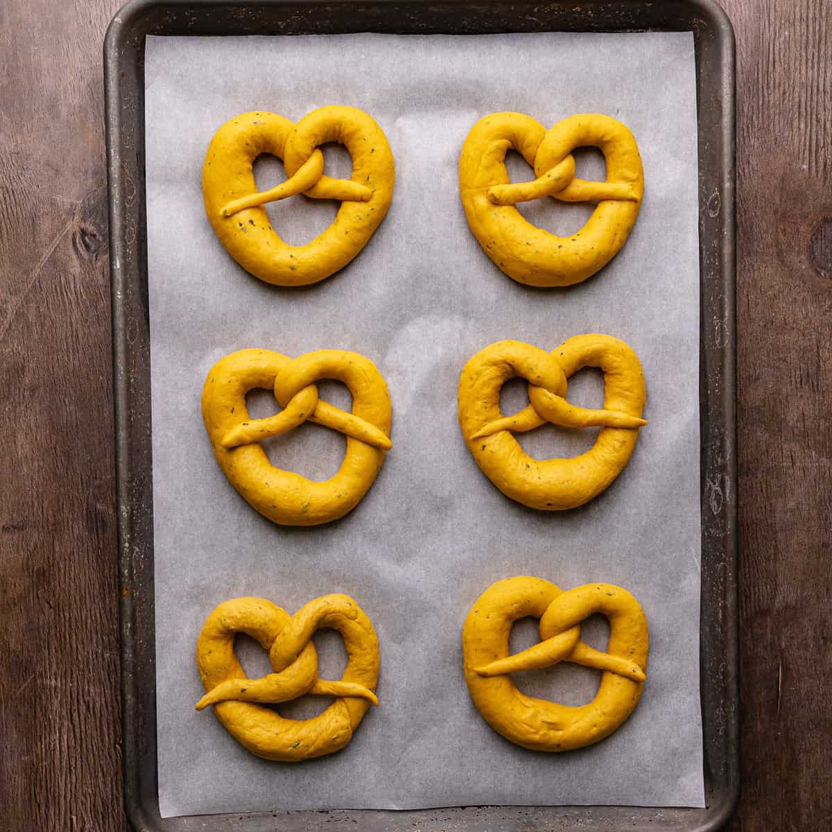 Soft pumpkin sage pretzels are shaped and then placed on a parchment lined baking sheet.