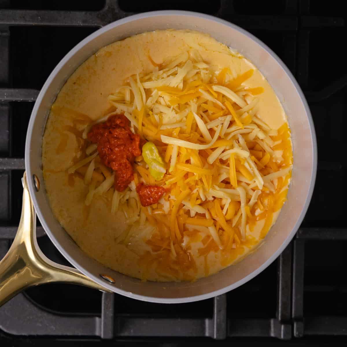 Shredded cheddar cheese, shredded gouda, hot chili pepper spread and mustard is added to the pot.
