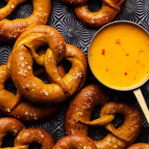 Soft pumpkin sage pretzels are topped with flaky sea salt and baked until golden brown and shiny and served with a spicy cheese beer dip.