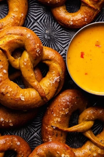 Soft pumpkin sage pretzels are topped with flaky sea salt and baked until golden brown and shiny and served with a spicy cheese beer dip.