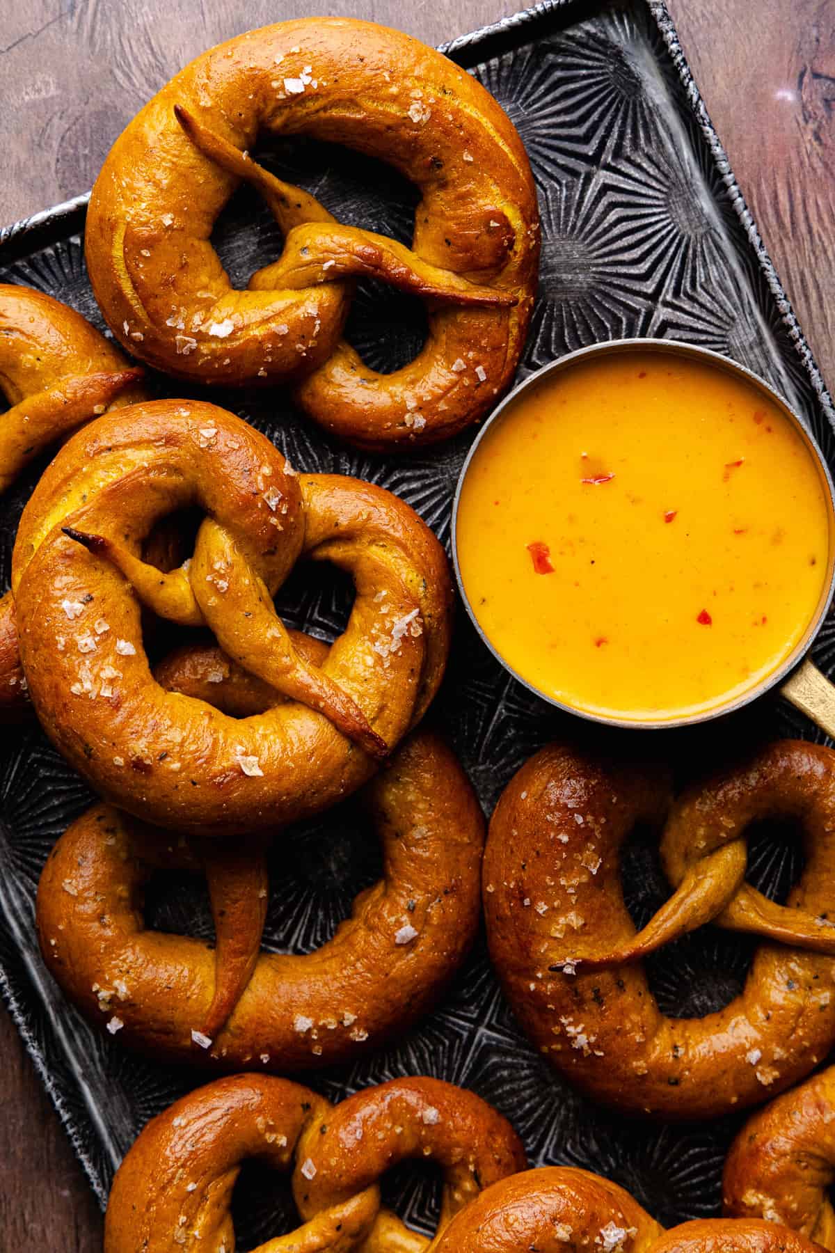 Soft pumpkin sage pretzels are topped with flaky sea salt and baked until golden brown and shiny and served with a spicy cheese beer dip.