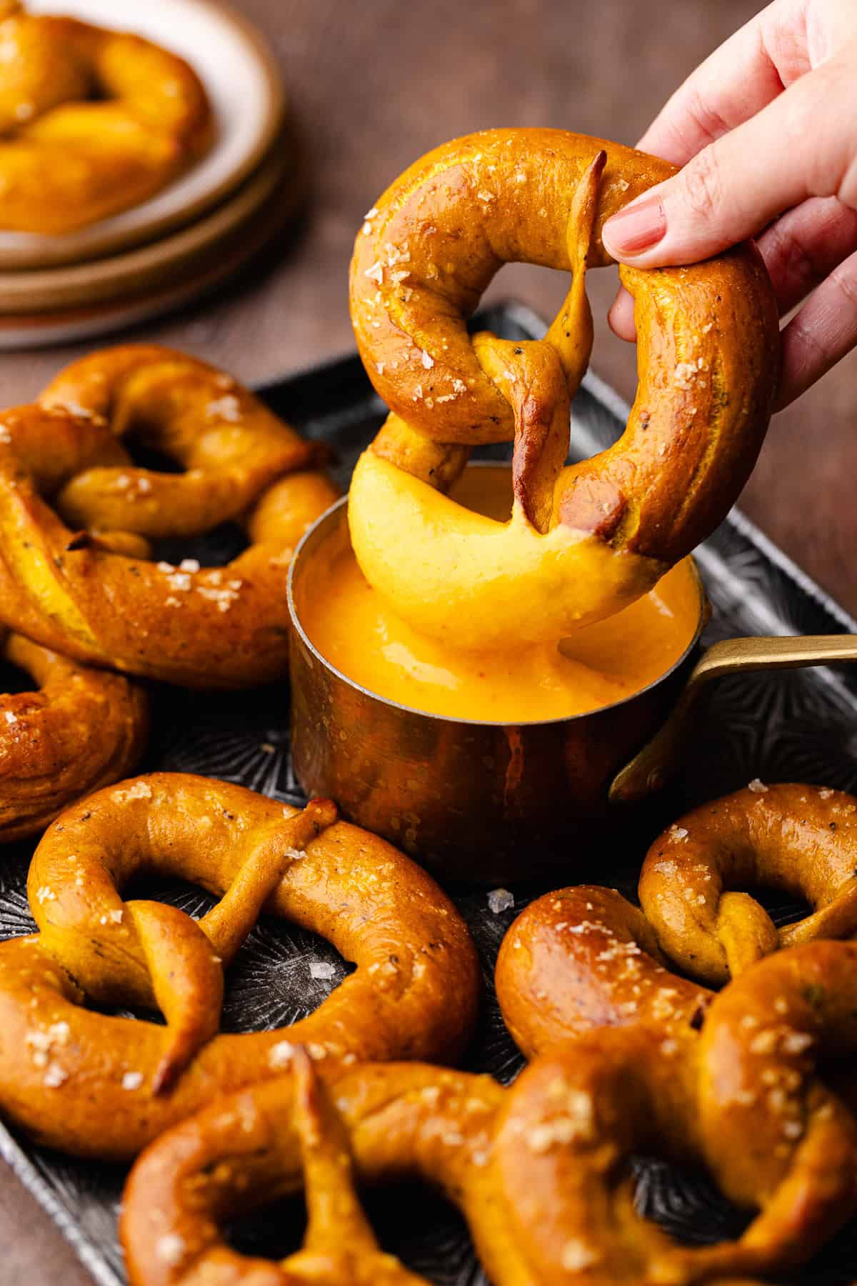 Soft pumpkin sage pretzels are topped with flaky sea salt and baked until golden brown and shiny and dipped in a spicy cheese beer sauce.