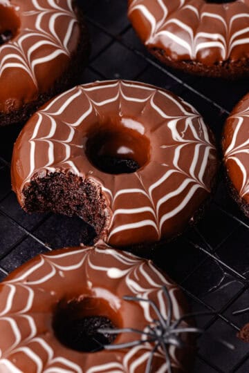 Spider web decorated baked chocolate donuts are sitting on a baking sheet with fake spiders all around.