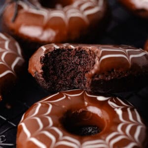Spider web decorated baked chocolate donuts are sitting on a baking sheet with fake spiders all around.