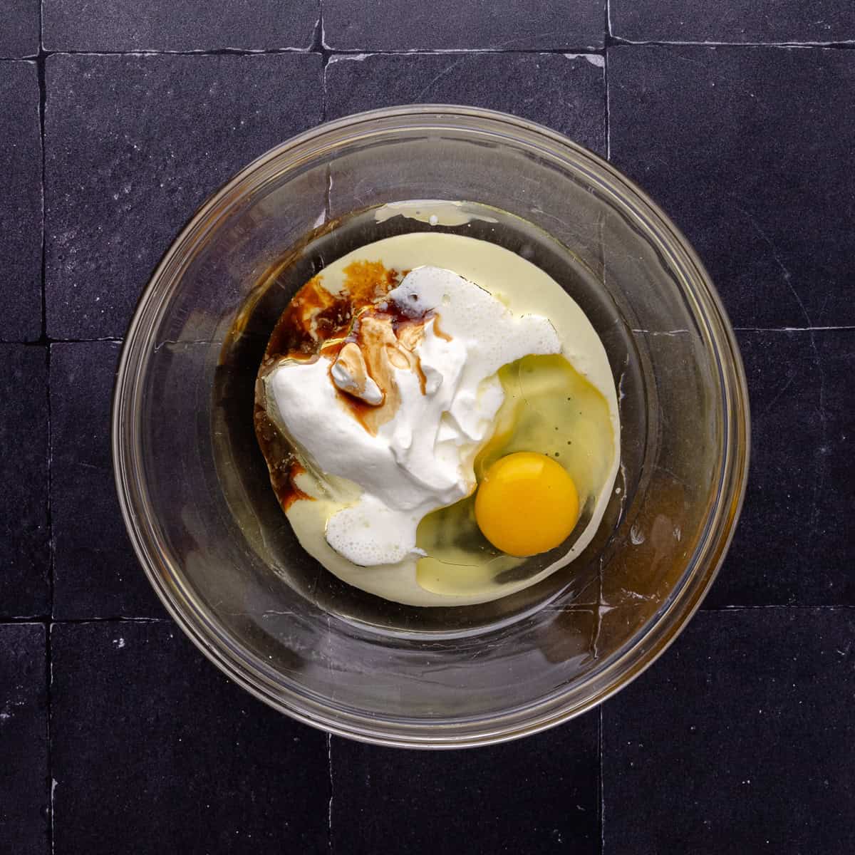 Olive oil, sour cream, buttermilk, an egg and vanilla are in a mixing bowl.