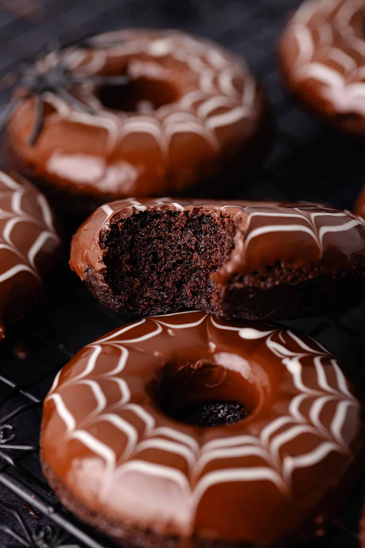 Spider web decorated baked chocolate donuts are sitting on a baking sheet with fake spiders all around.