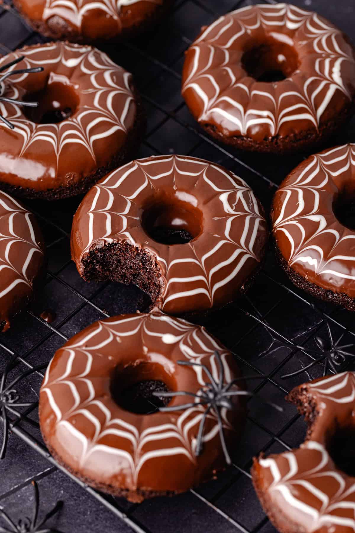 Spider web decorated baked chocolate donuts are sitting on a baking sheet with fake spiders all around.