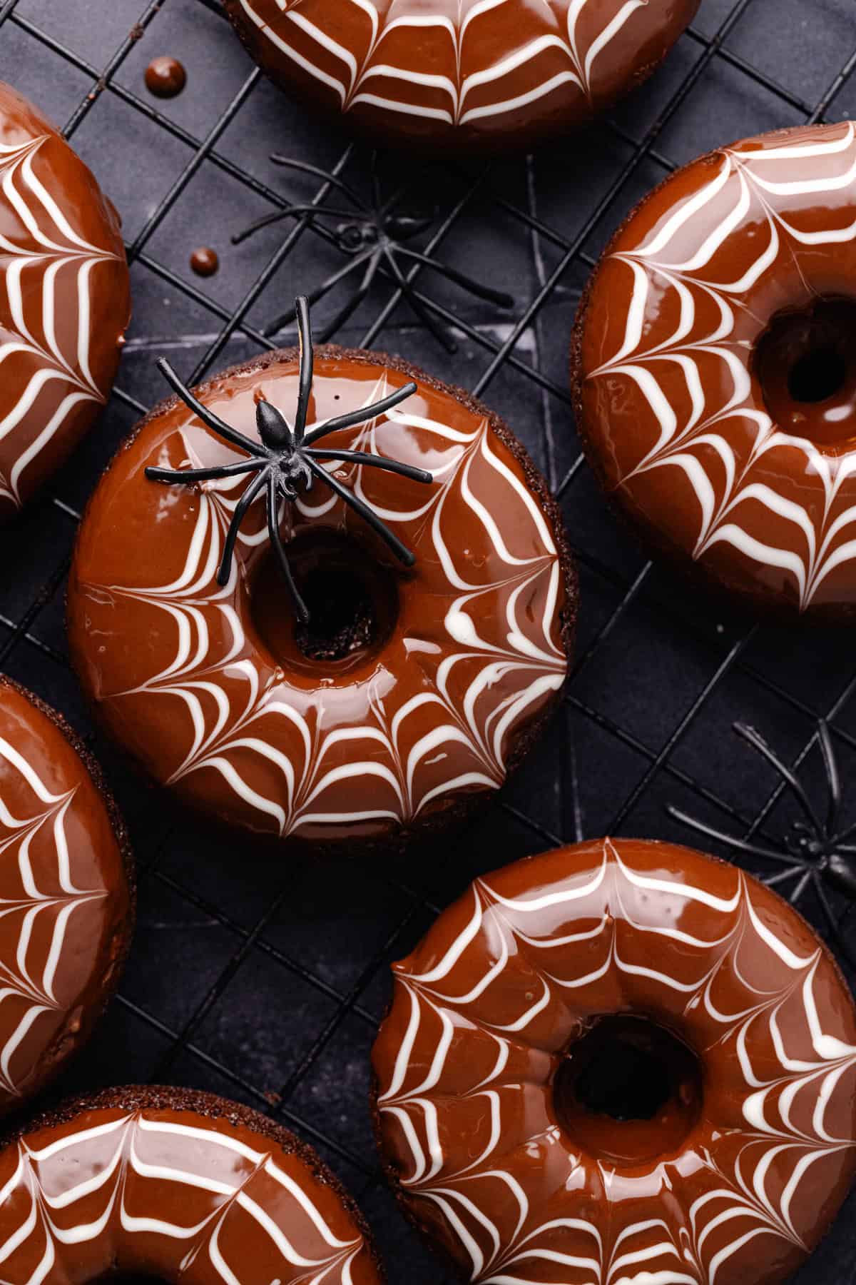 Spider web decorated baked chocolate donuts are sitting on a baking sheet with fake spiders all around.